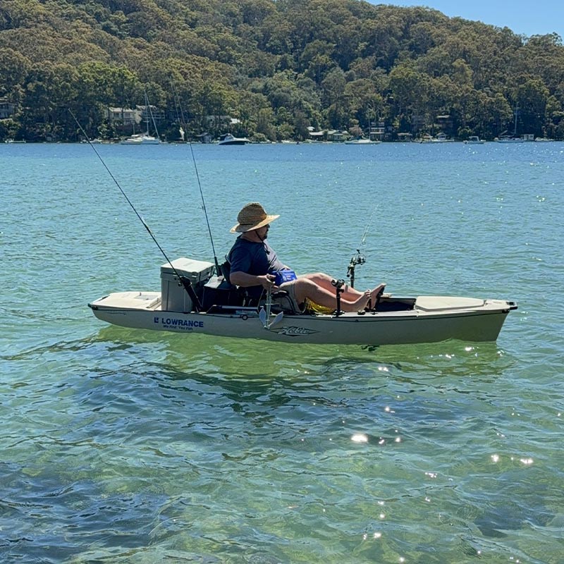 Person fishing in a small boat on a calm lake with trees in the background